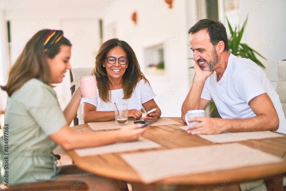 Beautiful family sitting on terrace drinking cup of coffee using smartphone speaking and smiling Beautiful family sitting on terrace drinking cup of coffee using smartphone speaking and smiling