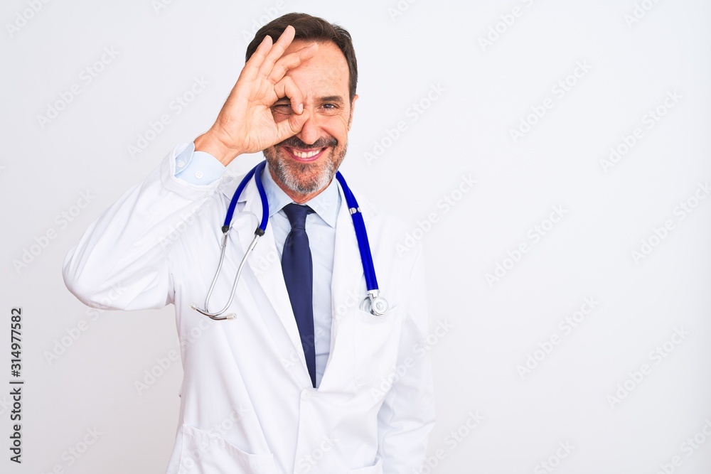 Middle age doctor man wearing coat and stethoscope standing over isolated white background doing ok gesture with hand smiling, eye looking through fingers with happy face. Middle age doctor man wearing coat and stethoscope standing over isolated white background doing ok gesture with hand smiling, eye looking through fingers with happy face.