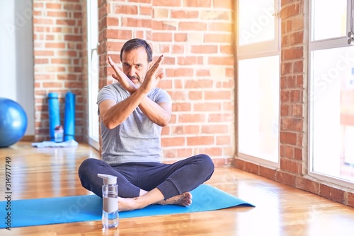 Middle age handsome sportman sitting on mat doing stretching yoga exercise at gym Rejection expression crossing arms doing negative sign, angry face