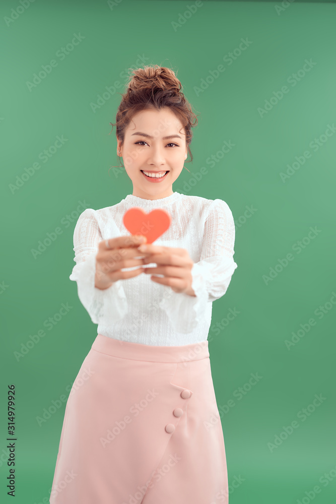 Cheerful young Asian woman holding red heart paper isolated over green background. Cheerful young Asian woman holding red heart paper isolated over green background.