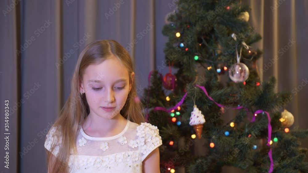 Young girl blowing up cracker on Christmas tree background in living room. Scared girl teenager exploding flapper on New Year celebrate on decorative tree background Young girl blowing up cracker on Christmas tree background in living room. Scared girl teenager exploding flapper on New Year celebrate on decorative tree background