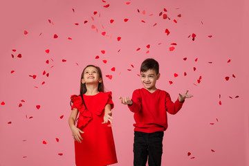 Happy romantic little couple child girl and boy stand in the rain of flying rose petals on pink background. St. Valentine's Day