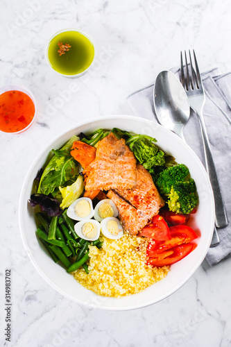 Healthy meal, keto food concept. Fish salad bowl on marble table background. Salad with salmon, couscous, vegetables, quail eggs. Top view, copy space