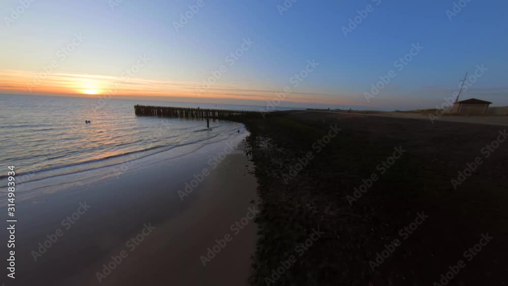 High to low angle aerial shot of a beach going towards a pier in the sea. High to low angle aerial shot of a beach going towards a pier in the sea.