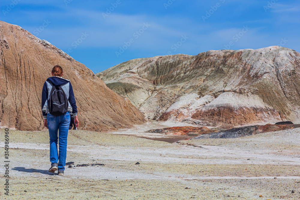 Landscape like a planet Mars surface. Young woman goes to Ural refractory clay quarries. Nature of Ural mountains, Russia. Solidified red-brown black Earth surface. Hiking concept