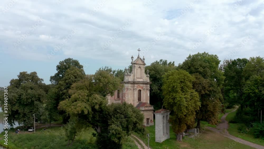 Hodovytsya, Ukraine - Front View Of The Ruins Of The Old All Saints Catholic Church Surrounded By Lush Trees On A Cloudy Day  - Aerial Drone Shot