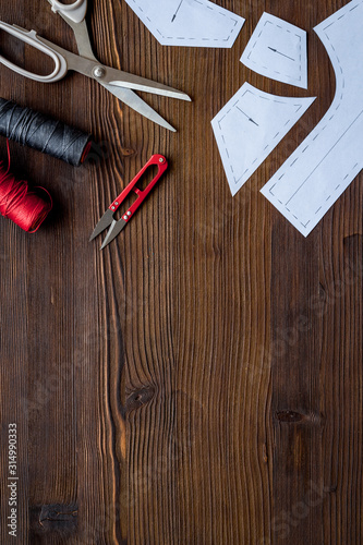 Clothes designer work desk. Pattern, scissors, thread on dark wooden background top-down copy space