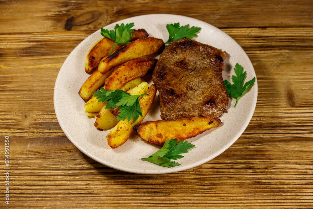 Fried beef steak with potato wedges on wooden table