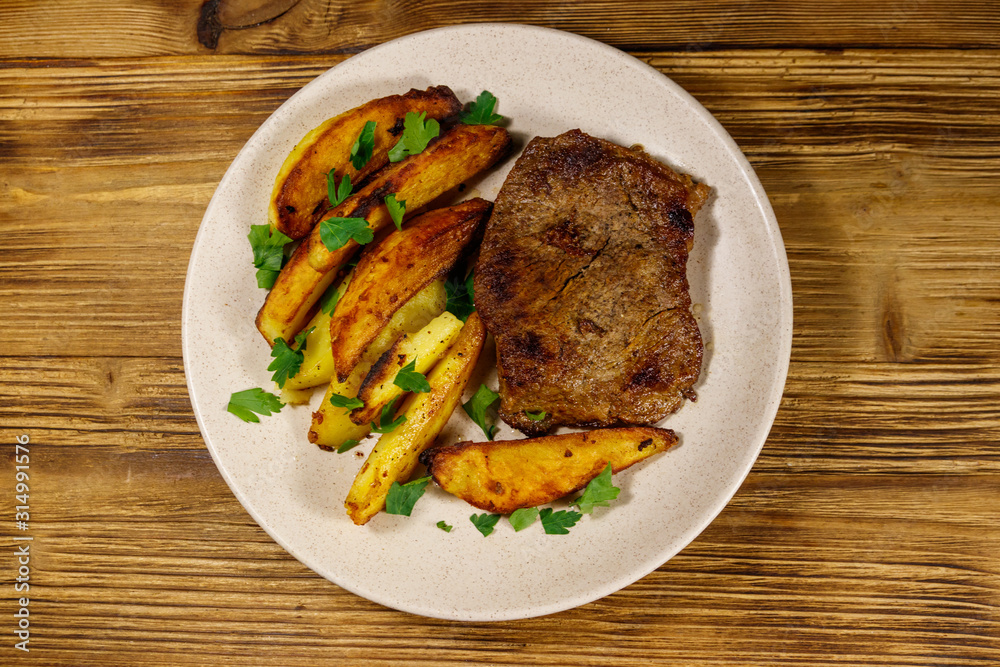 Fried beef steak with potato wedges on wooden table. Top view