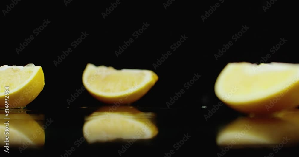 One juicy sliced ​​yellow lemon falling on a glass with splashes of water in slow motion on a dark background.