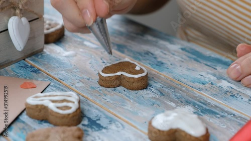 Woman decorating ginger cookies heart shaped for valentine day or christmas, covering with white glaze, close up photo