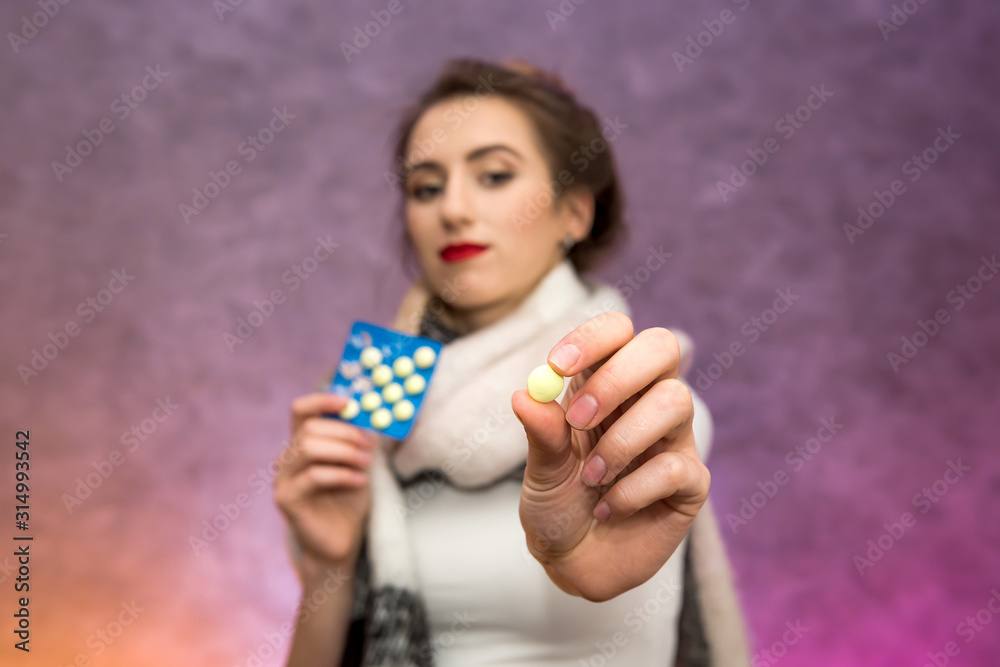 Tired woman with warm scarf on neck and pills in blister posing on abstract background. Illness concept