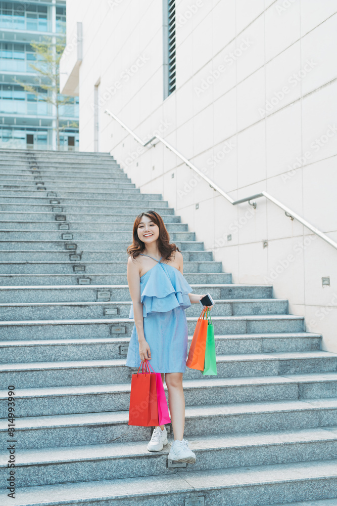 Asian young smile woman enjoy shopping with colorful bag while going down stairs.