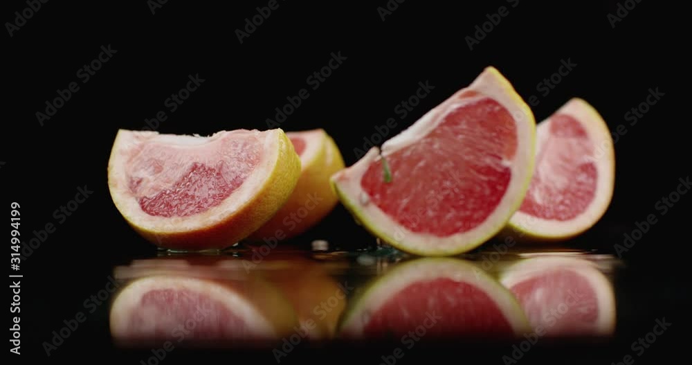 One juicy sliced ​​grapefruit falling on a glass with water splashes in slow motion on a dark background.