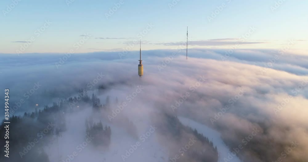 Majestic 4K drone shot with parallax motion of Oslo winter sport park and telecom tower on top of mountain, with fast moving clouds fog in orange golden sunset, in Tryvann Holmenkollen Oslo Norway. Majestic 4K drone shot with parallax motion of Oslo winter sport park and telecom tower on top of mountain, with fast moving clouds fog in orange golden sunset, in Tryvann Holmenkollen Oslo Norway.
