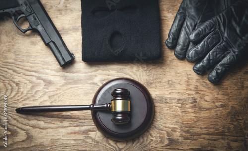 Judge hammer, pistol, mask, gloves on wooden background.