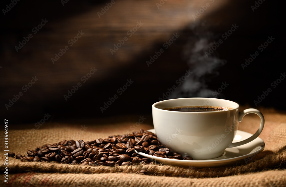 Cup of coffee with smoke and coffee beans on burlap sack on old wooden background