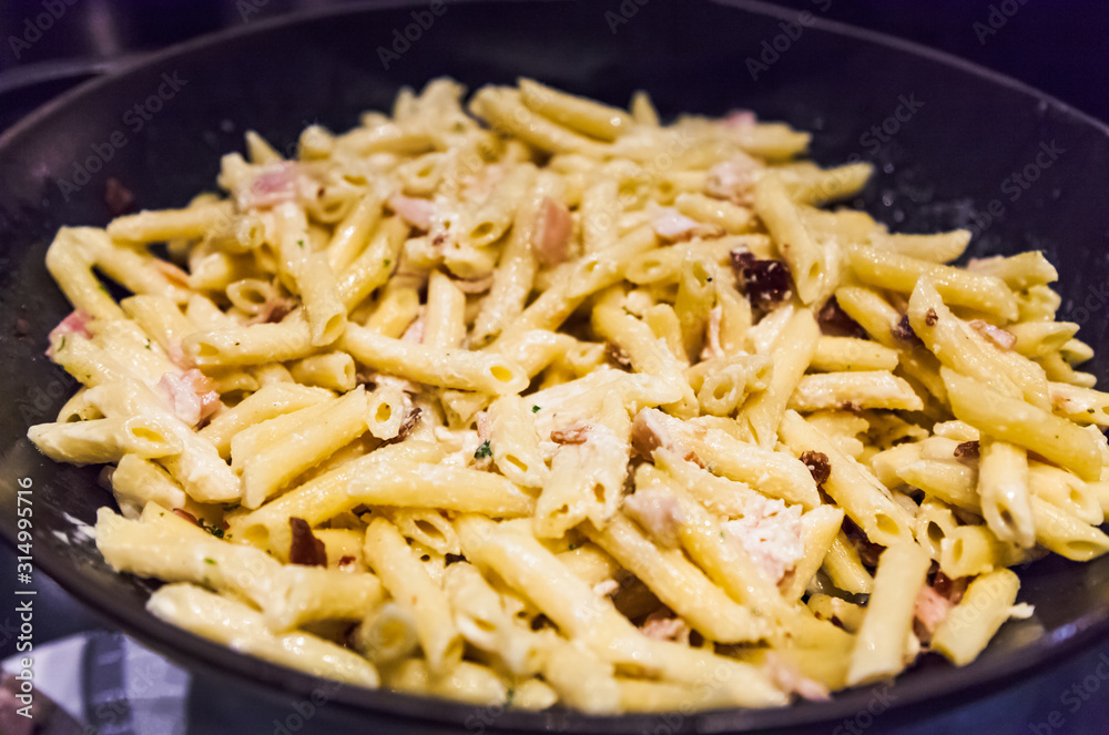 Delicious Creamy White Sauce Hearty Bacon Garlic Penne Pasta in frying skillet pan. Italian Pasta Dish, Gastronomy, Delicacy, Cuisine, Food, Meal, Dinner and Recipe concept Delicious Creamy White Sauce Hearty Bacon Garlic Penne Pasta in frying skillet pan. Italian Pasta Dish, Gastronomy, Delicacy, Cuisine, Food, Meal, Dinner and Recipe concept