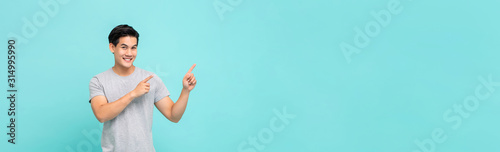 Cheerful smiling young Asian man pointing hands to copy space aside