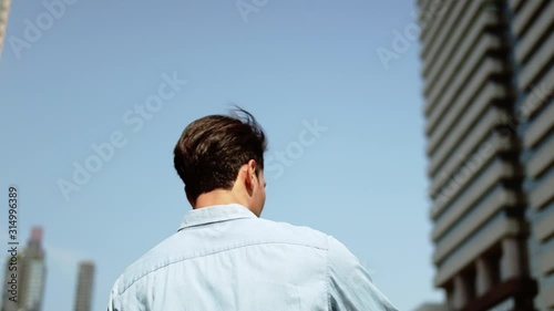 a Young Man Using Mobile Phone in Urban City. Low Angle View. Slow Motion. Modern Building as background