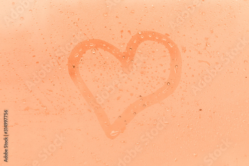 The child picture or figure of the heart on the orange or pink evening or morning window glass with drops 