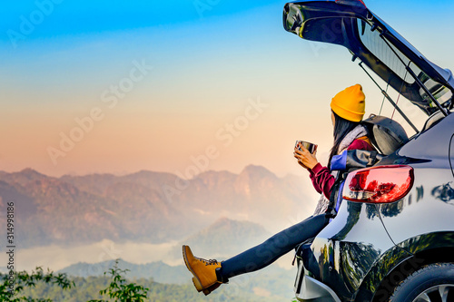 Woman traveller enjoy coffee time on back storage of car with scenery view of the mountain and mist morning in background photo