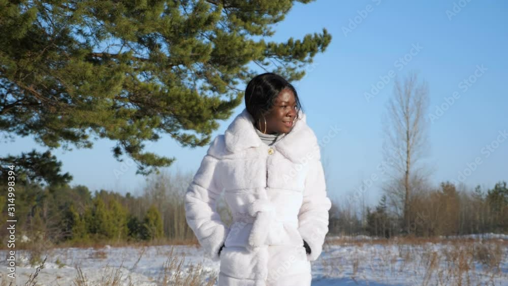 beautiful dark-skinned woman in white fur coat walks along snowy forest meadow enjoying nature on sunny day slow motion beautiful dark-skinned woman in white fur coat walks along snowy forest meadow enjoying nature on sunny day slow motion