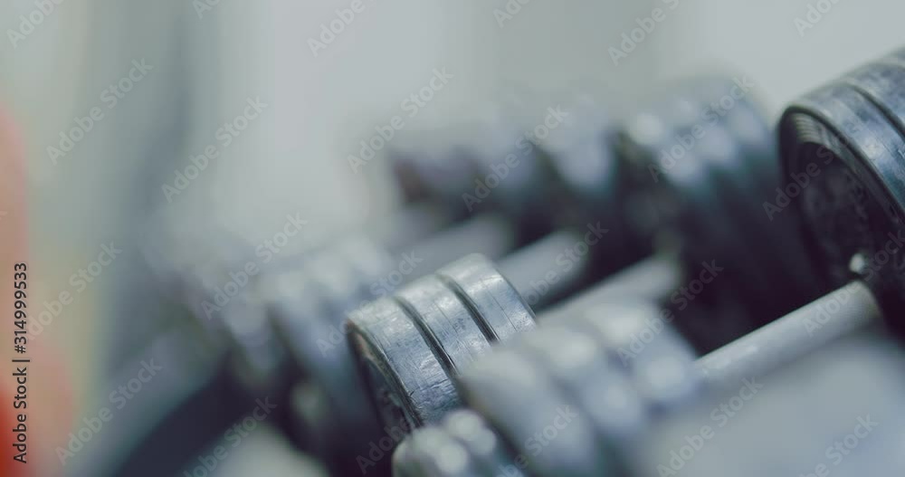 Female hand takes a metal dumbbell from the rack, sports equipment of the gym. Close-up. Female hand takes a metal dumbbell from the rack, sports equipment of the gym. Close-up.
