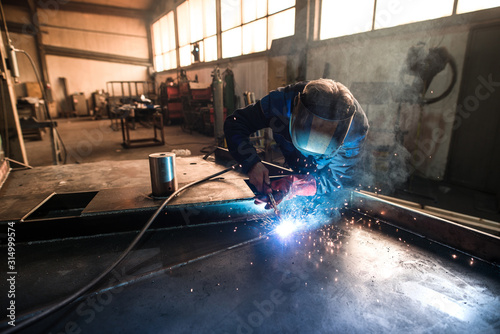 Professional welder welding metal construction parts in industrial workshop. An experienced worker joining iron parts using MIG welding technique.