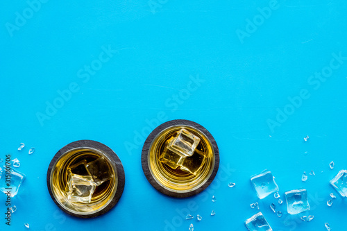 Whiskey near ice cubes on blue background top-down frame copy space