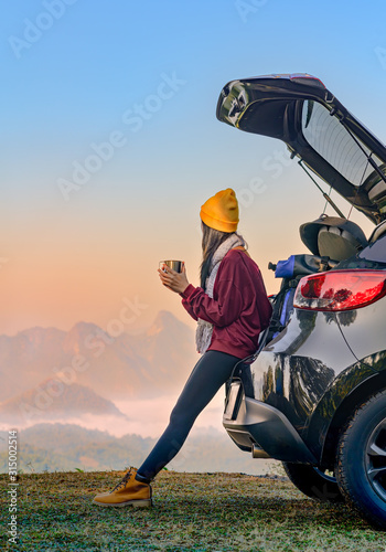Woman traveller enjoy coffee time on back storage of car with scenery view of the mountain and mist morning in background