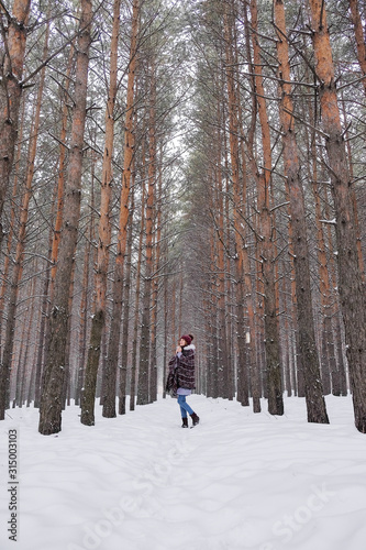 Portrait of a girl in a warm gray coat and burgundy knit scarf in the winter woods.