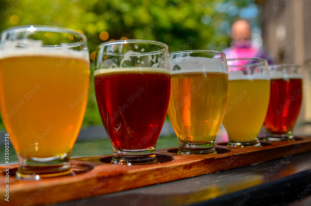 Craft beer tasting: five glasses with beers of different colors and flavors. A wooden cup holder holds the glasses in a row. Craft beer tasting: five glasses with beers of different colors and flavors. A wooden cup holder holds the glasses in a row.