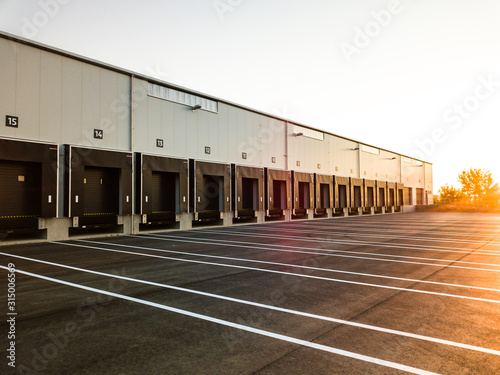 Canvas Print Warehouse exterior with loading ramps and slots for trucks to park - modern industry warehouse storage building