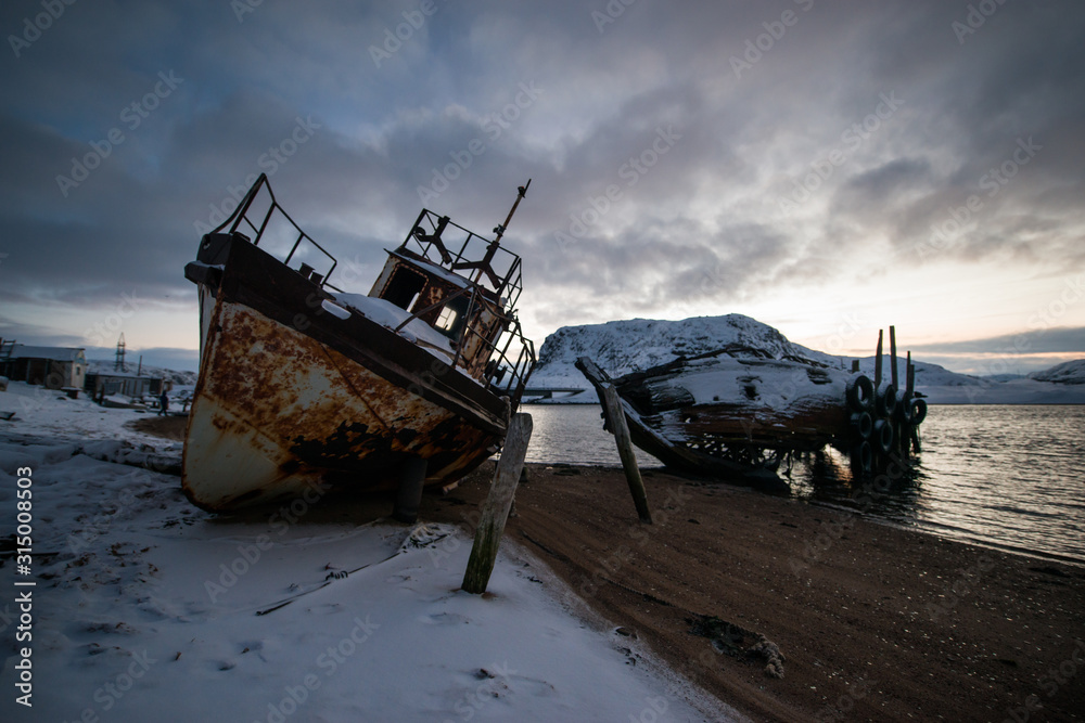 abandoned, already rotten skeletons of ships lying on the coast of the Arctic ocean against the background of a pink sunset