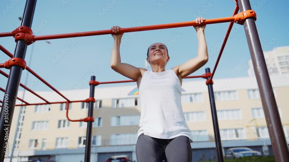 Female athlete doing pull-ups on horizontal bar outdoors.