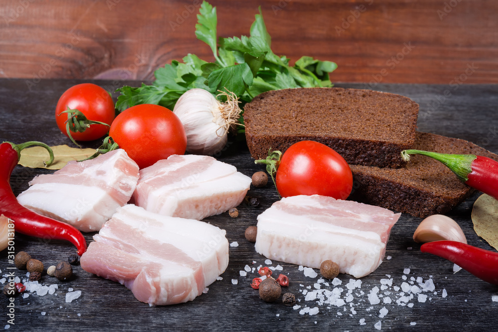 Pork belly slices, against the spices, vegetables, brown bread, closeup