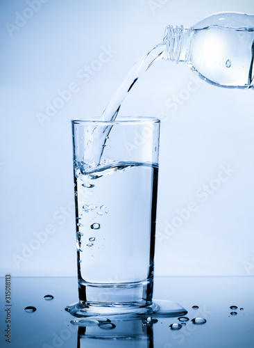 Foto Pouring fresh pure water from bottle into a glass on the table with water drops,