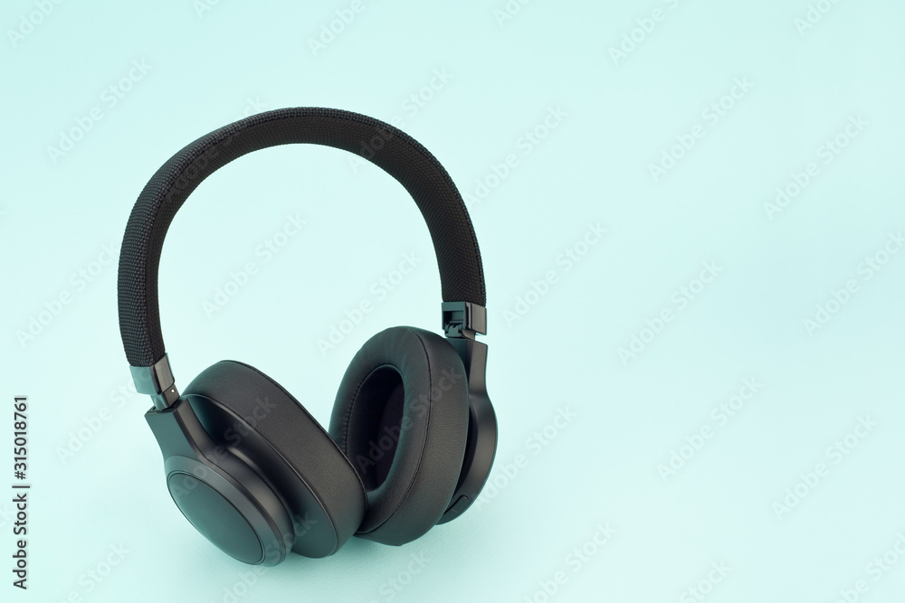 Modern wireless black headphones on a light blue background. Modern wireless black headphones on a light blue background.