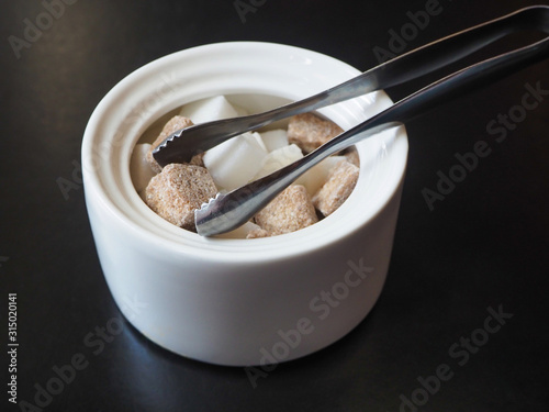 Sugar-basin with cubes of white and brown sugar on black background