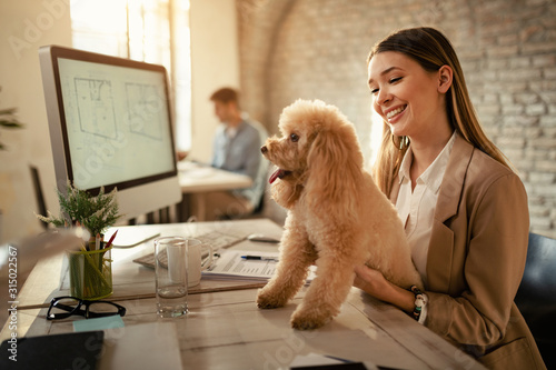 Happy businesswoman enjoying with her dog while working in the office.