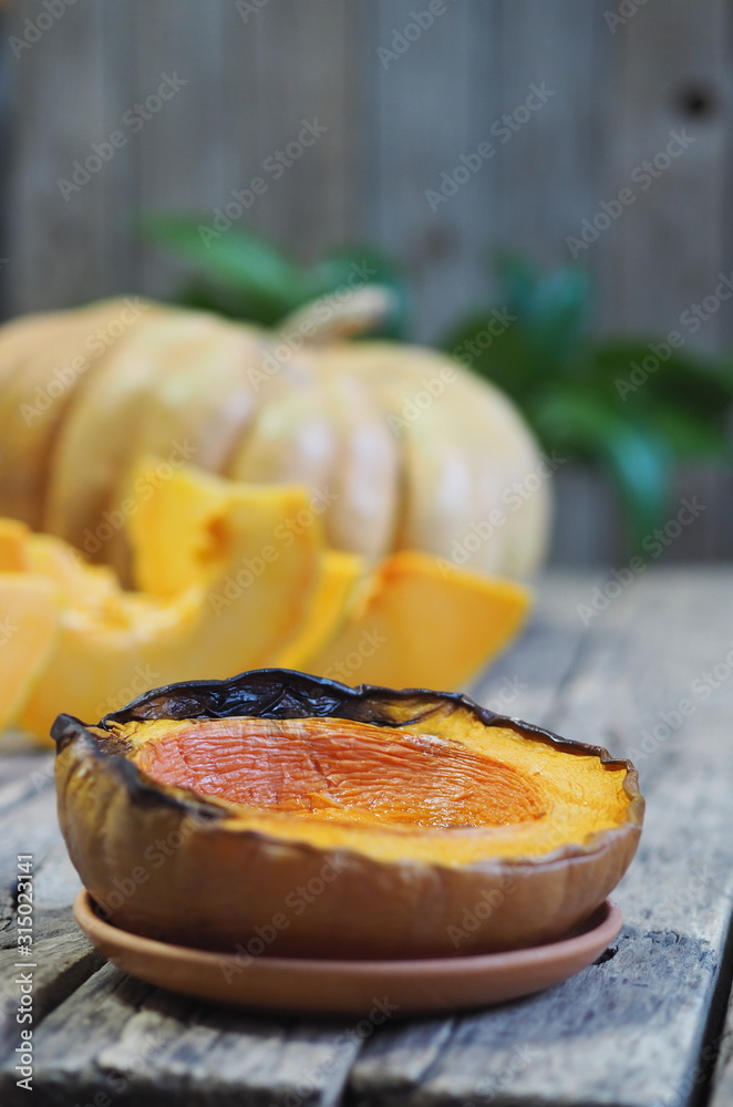 Cooking pumpkins. Home cooking, natural food for vegetarians. Traditional autumn pumpkin dishes. Grilled grilled pumpkin with spices on a background of raw whole pumpkin on a wooden background.