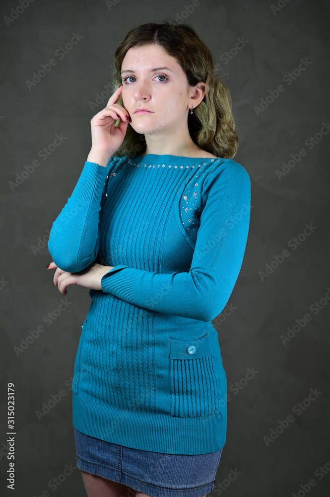 Portrait of a pretty student girl with beautiful curly hair is standing in front of the camera on a gray background. Concept vertical photo of a young woman with emotions in a blue dress. Portrait of a pretty student girl with beautiful curly hair is standing in front of the camera on a gray background. Concept vertical photo of a young woman with emotions in a blue dress.