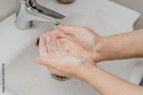 wash your hands with soap under the foam tap in the bathroom, hygiene, clean hands. the man washes his hands.