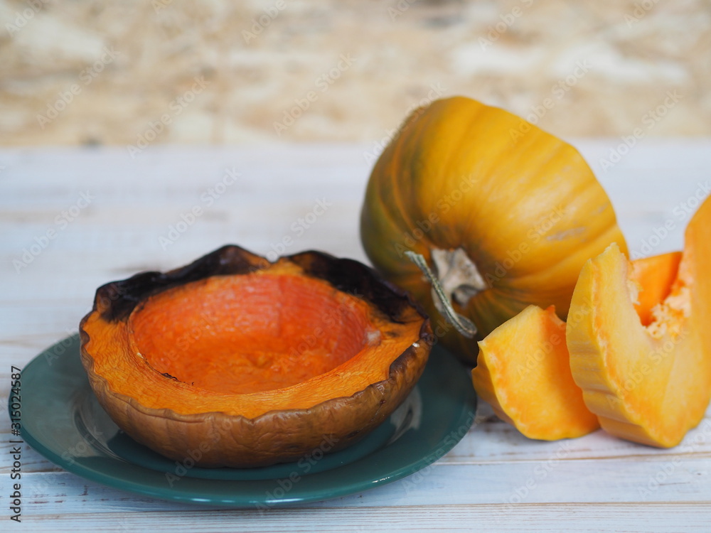 Cooking pumpkins. Home cooking, natural food for vegetarians. Traditional autumn pumpkin dishes. Grilled grilled pumpkin with spices on a background of raw pumpkin on a white wooden table.
