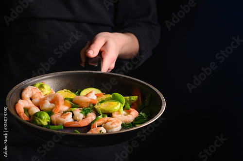 Wallpaper Mural Chef cooks shrimps with vegetables, in a pan with fire. Frying and cooking. Oriental cuisine. Culinary, restaurant business, healthy and tasty food. Banner, on black background. Torontodigital.ca