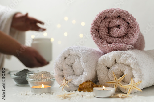 Spa salon concept. Woman with bowl of moisturizing cream, towels and glass bowls full of body clay, candles, sea salt on the white surface