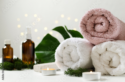 Natural spa procedures. Fresh tropical leaves, towels, candles and glass bottles of oil for body on the white surface against bokeh lights