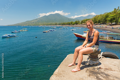 Beautiful young woman sits on a jetty and looks out over the blue sea of North Sulawesi, Indonesia