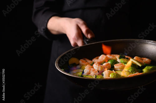 Professional cook cooks shrimps with vegetables on fire. Cooking seafood